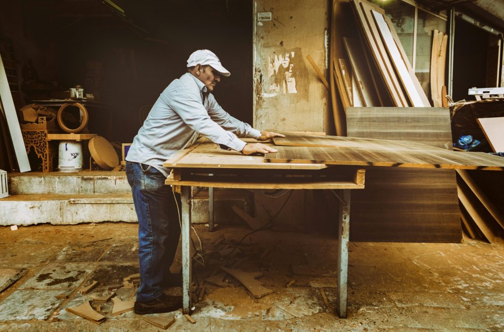ChatGPT said: Un artisan en train de travailler une grande planche de bois massif dans son atelier, entouré d’outils et de matériaux, illustrant le savoir-faire et l’authenticité du travail du bois.