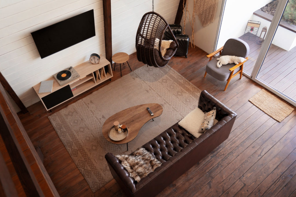Vue de dessus d'un salon chaleureux au style scandinave, avec un canapé en cuir marron, un fauteuil suspendu en rotin et du mobilier en bois massif